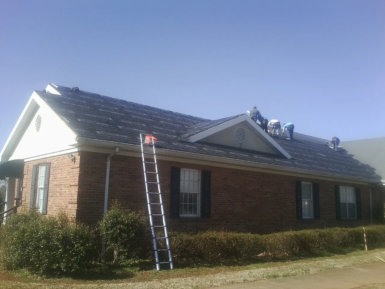 Crew tearing shingles off a brick ranch roof with a ladder set — Metal Roof Repair work by our crew in Broadway