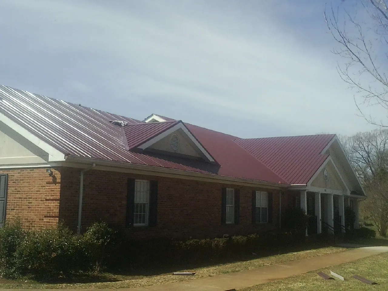 Red metal roof with gabled entries on a long brick building, from a Hail Damage Roof Repair job in Broadway